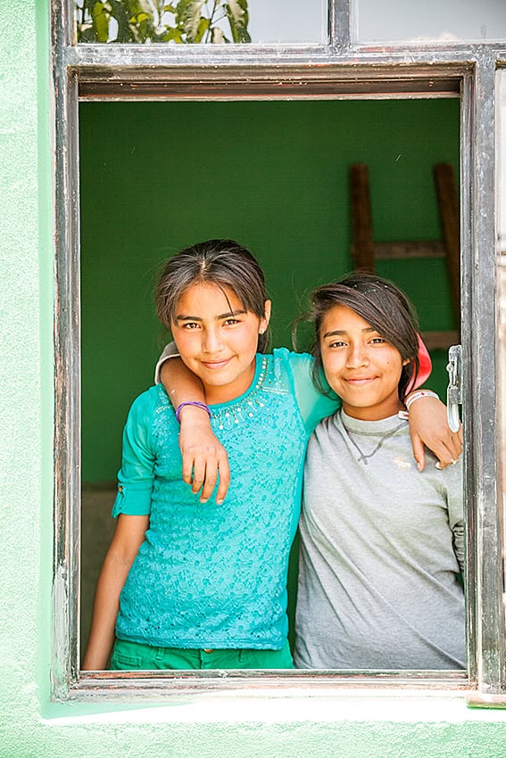 Niñas colegialas sonrientes se abrazan en una ventana abierta en San Miguel, enfatizando la educación y la comunidad.