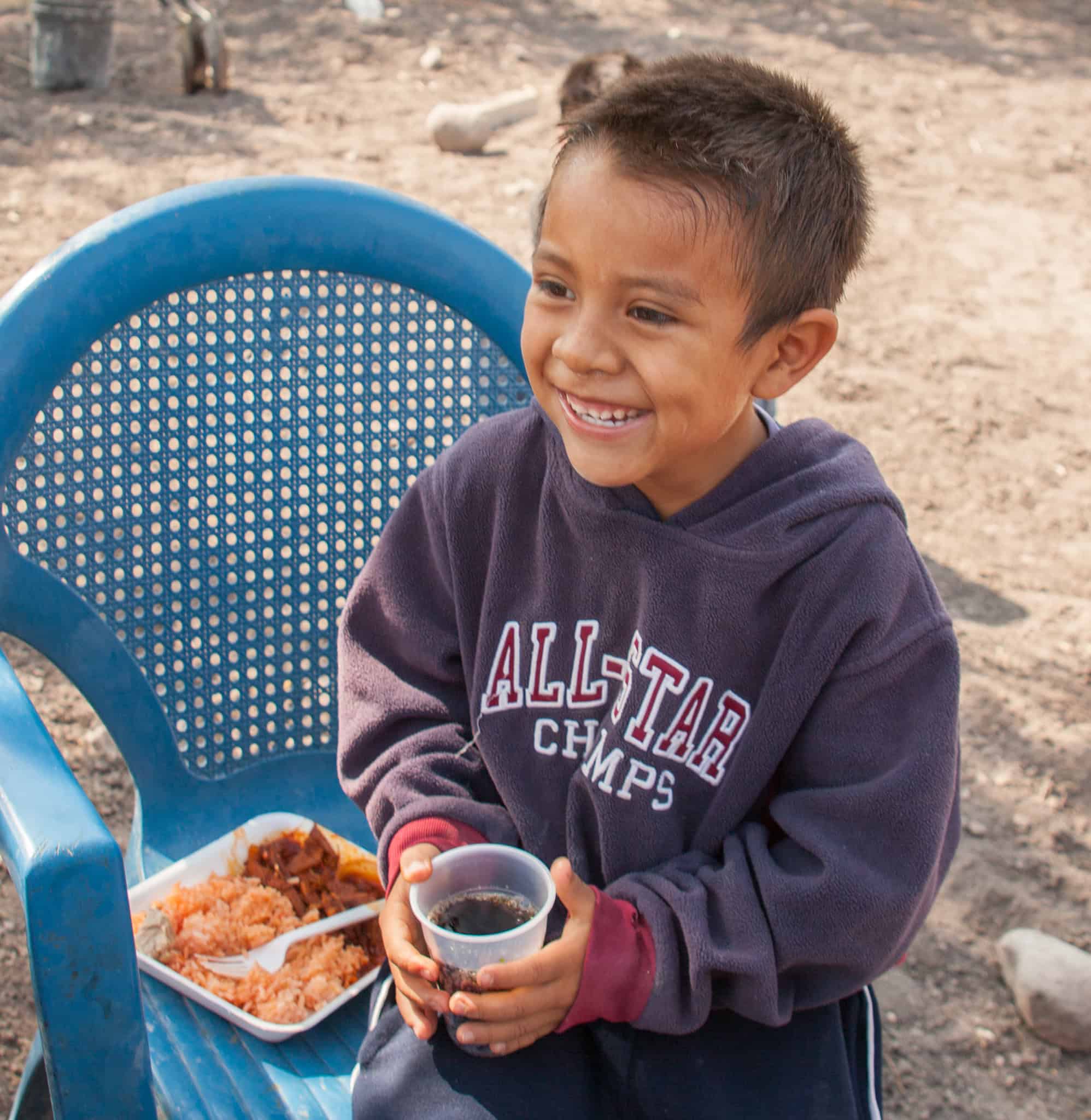 Niño feliz disfrutando de una comida al aire libre, sonriendo con comida y bebida en un día soleado en San Miguel.