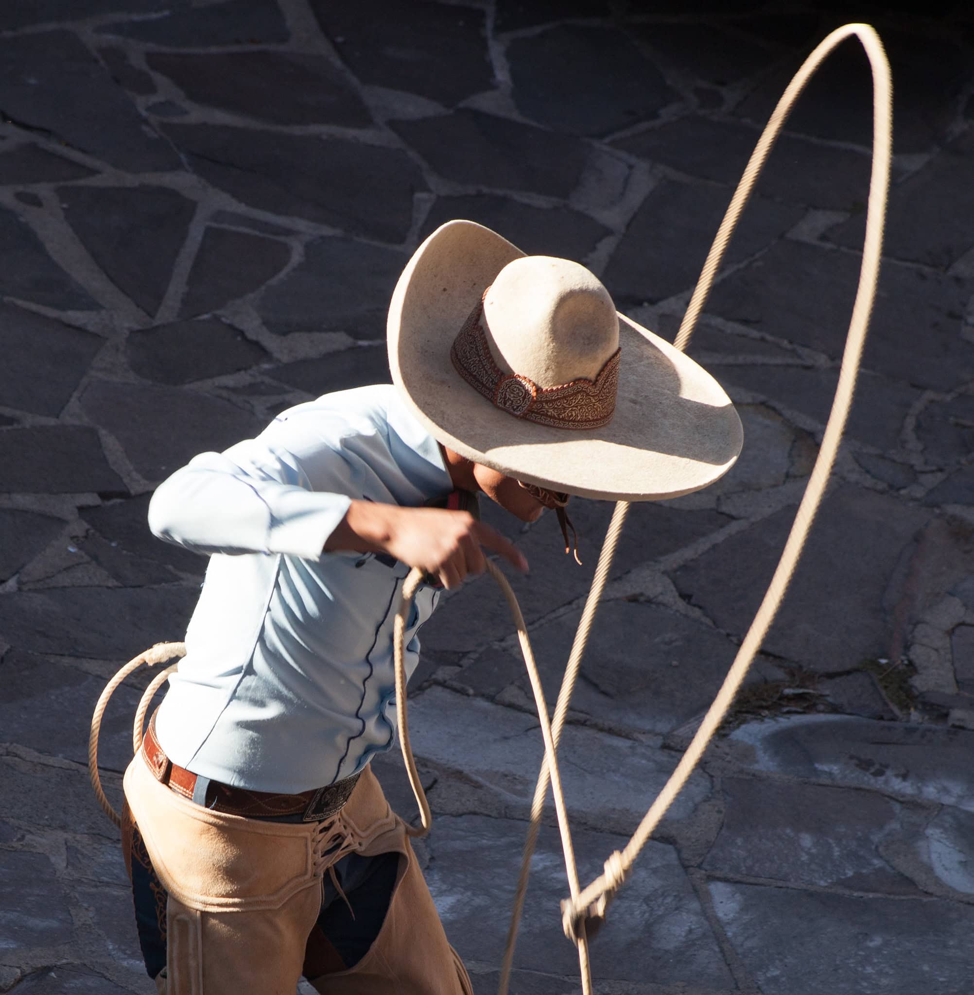 Colorful Mexican charro performer with a wide-brimmed hat and lasso, traditional attire at a San Miguel cultural event.