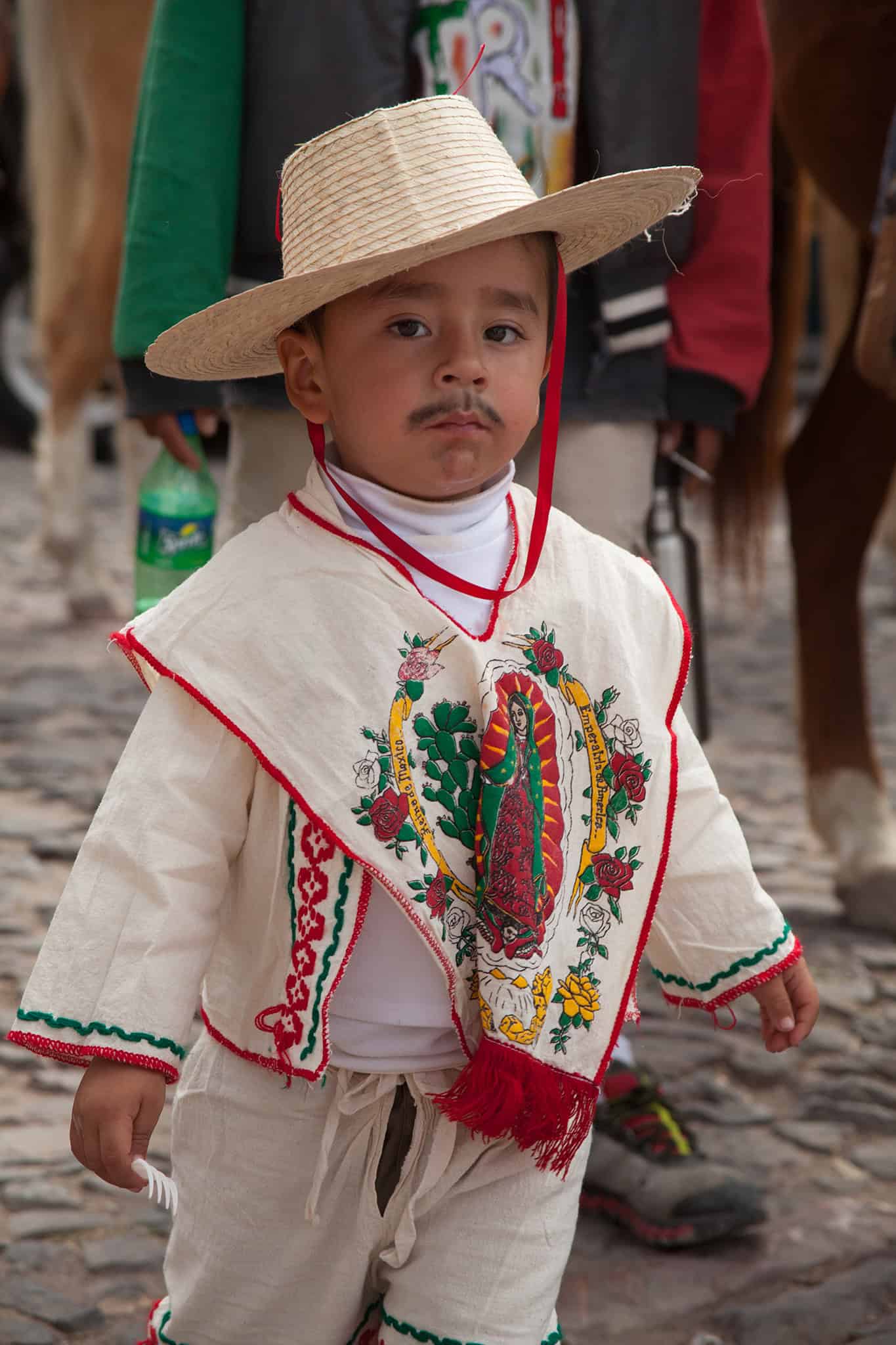 Mexican boy in traditional attire during a San Miguel de Allende cultural festivity with embroidered clothing and straw hat.