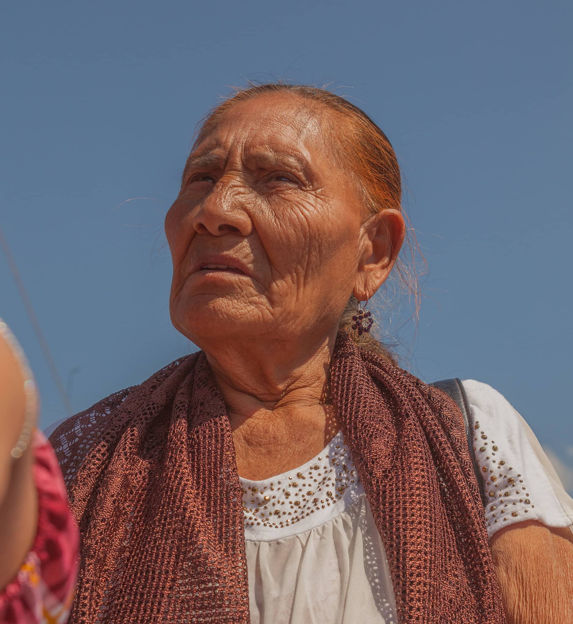 Elderly woman outdoors with a clear blue sky, portrait emphasizing age and San Miguel cultural heritage.