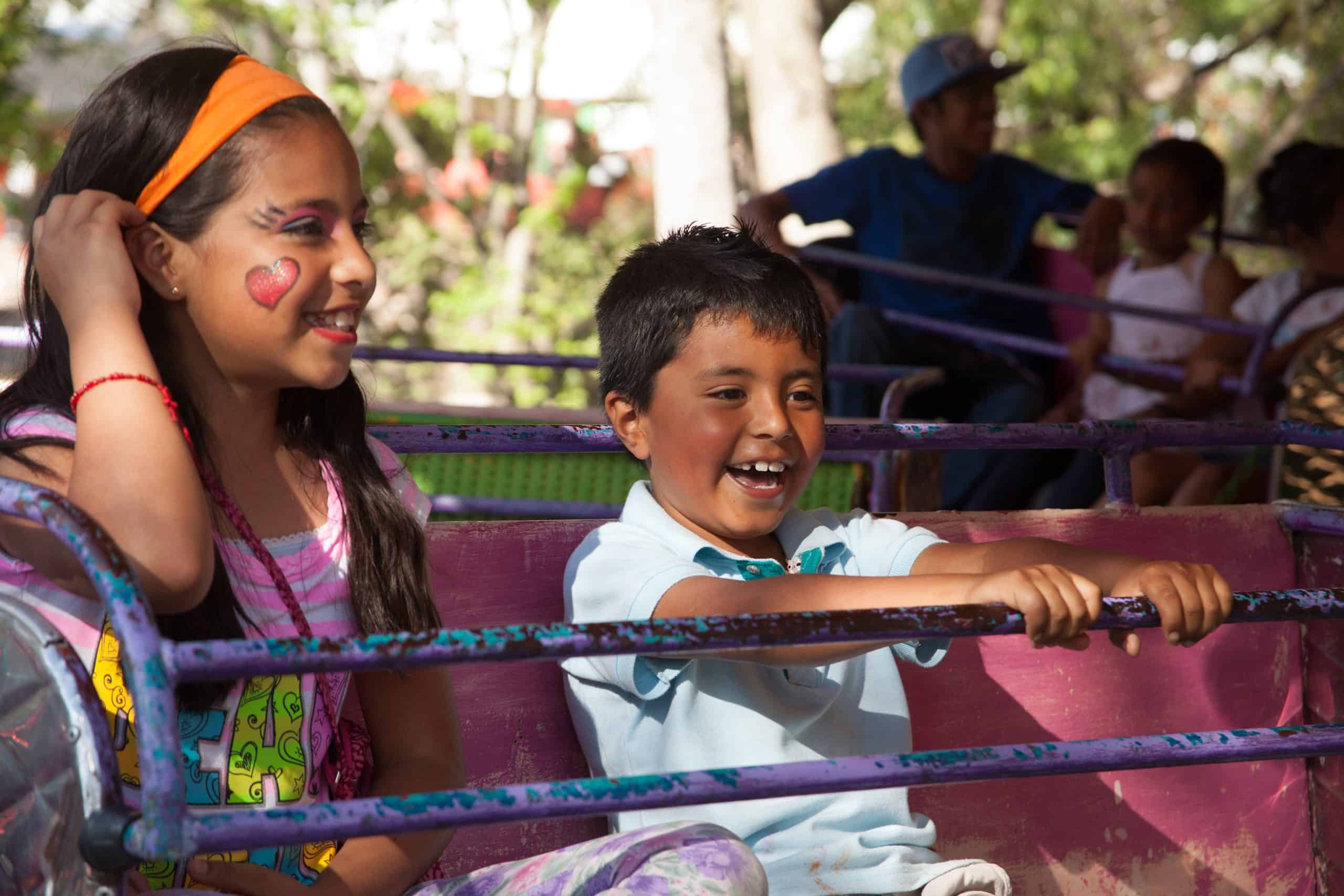 Bright smiling children enjoying a colorful amusement park ride in San Miguel filled with joyful laughter and childhood fun.