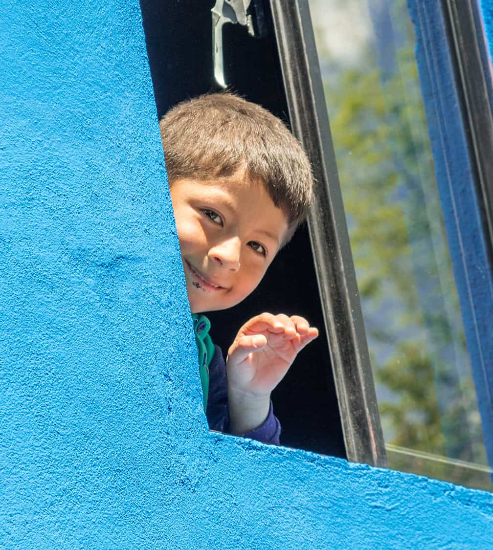 Happy young boy looking out of window on bus in San Miguel, enjoying travel, transportation, childhood, and innocence.