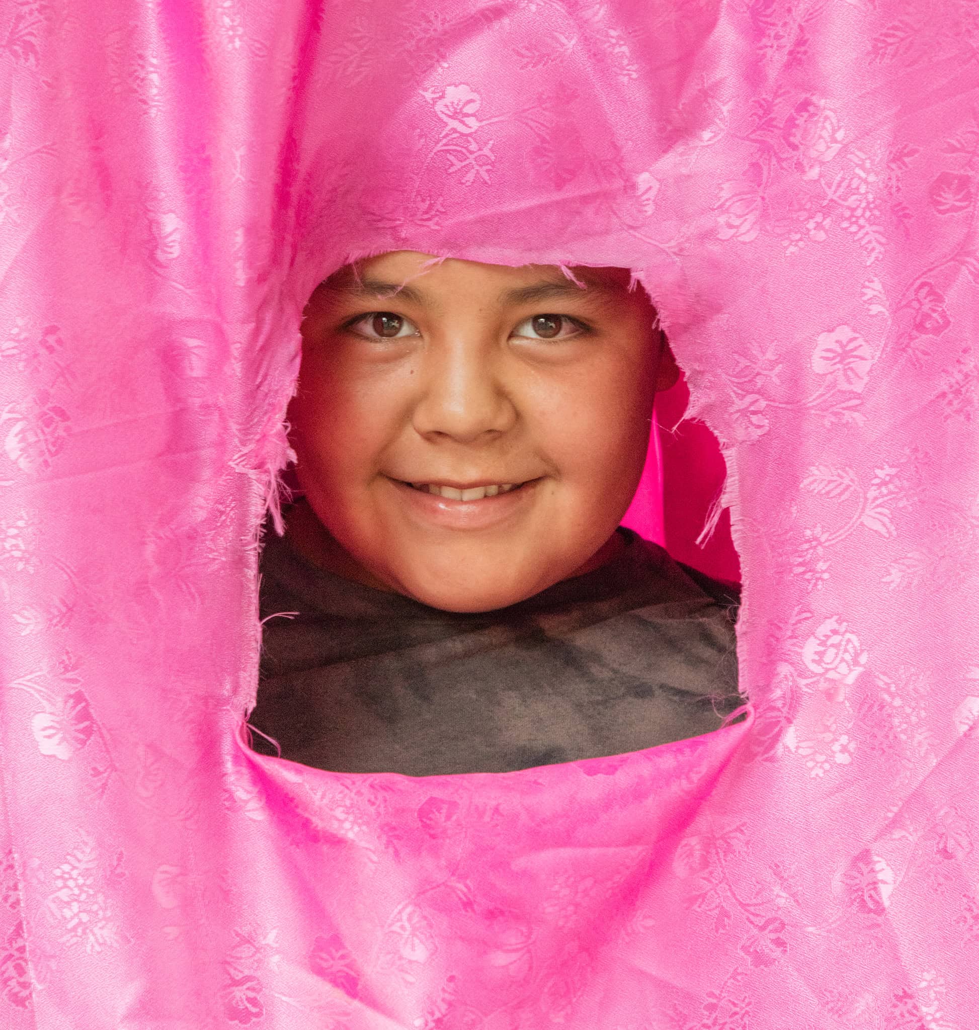Bright smiling boy peeking through pink floral fabric in San Miguel.