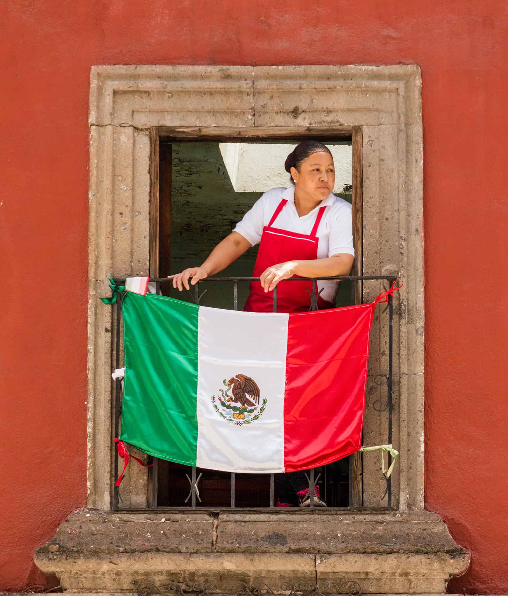 Mexico flag displayed on balcony with woman in traditional attire, celebrating local culture in San Miguel de Allende.