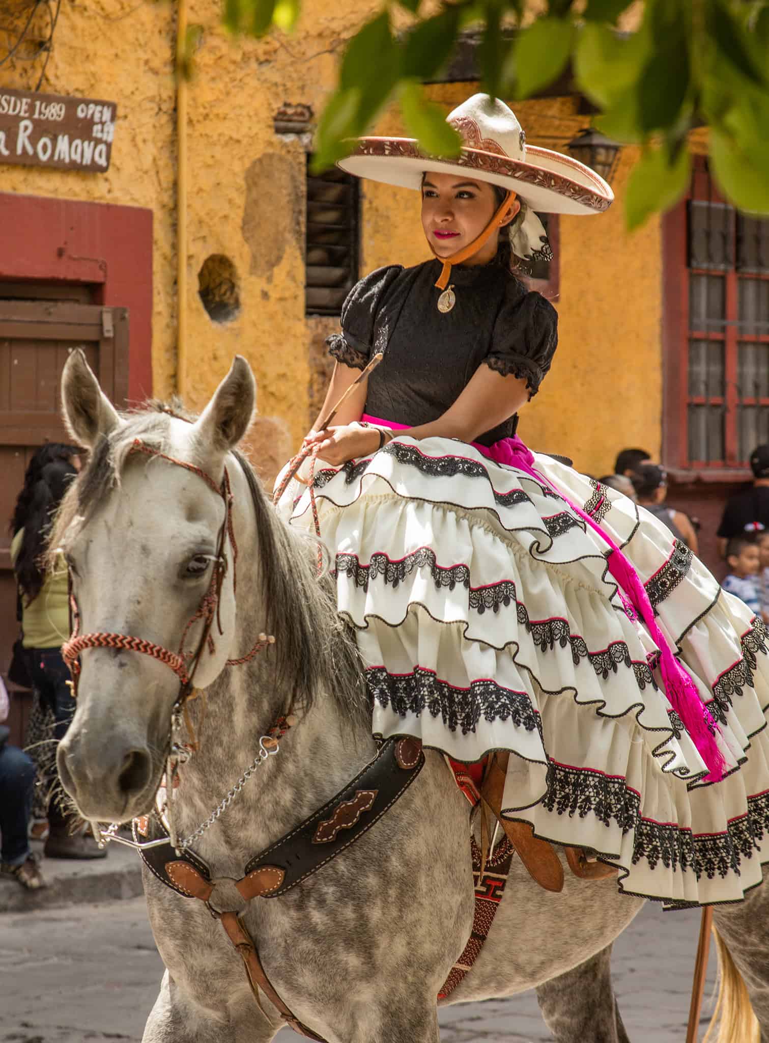 Vibrant Mexican woman riding a white horse in traditional dress for festival, showcasing San Miguel de Allende's rich cultural heritage.