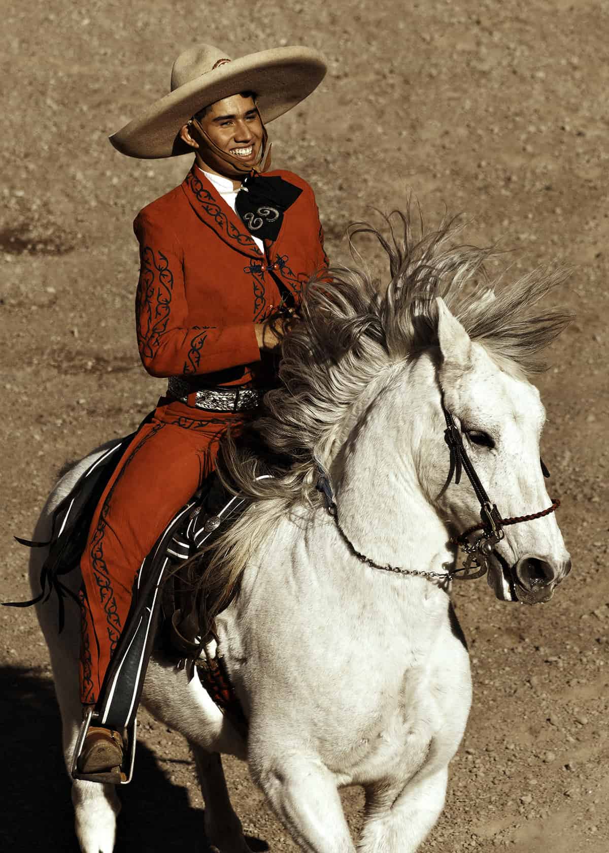 Young man in traditional Mexican charro outfit riding a white horse in San Miguel.