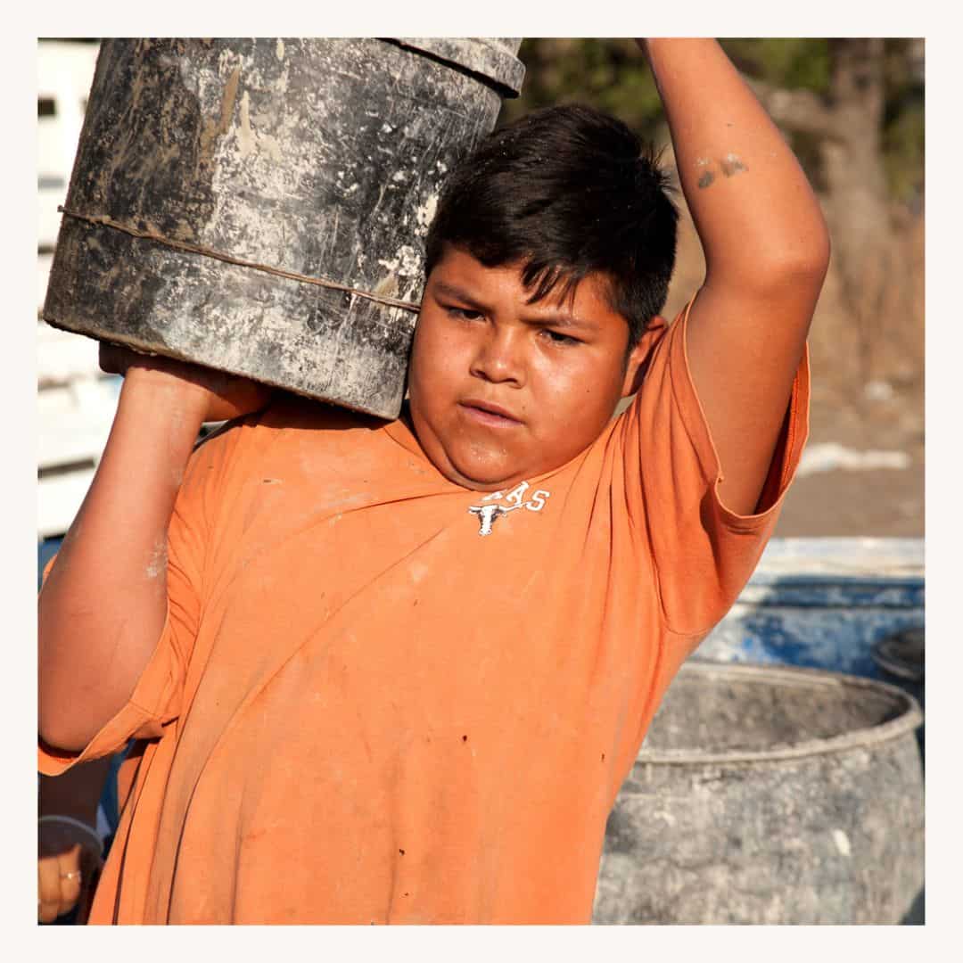 Child carrying a large bucket on his shoulder, featuring a SMCF Nonprofit Network Member organization.