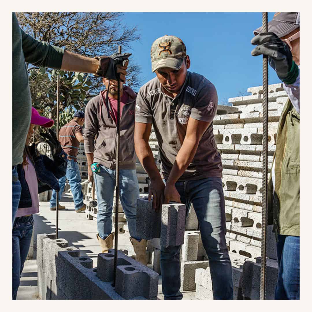 Construction workers laying concrete blocks for building walls, featuring the impact of a SMCF Nonprofit Network Member organization.