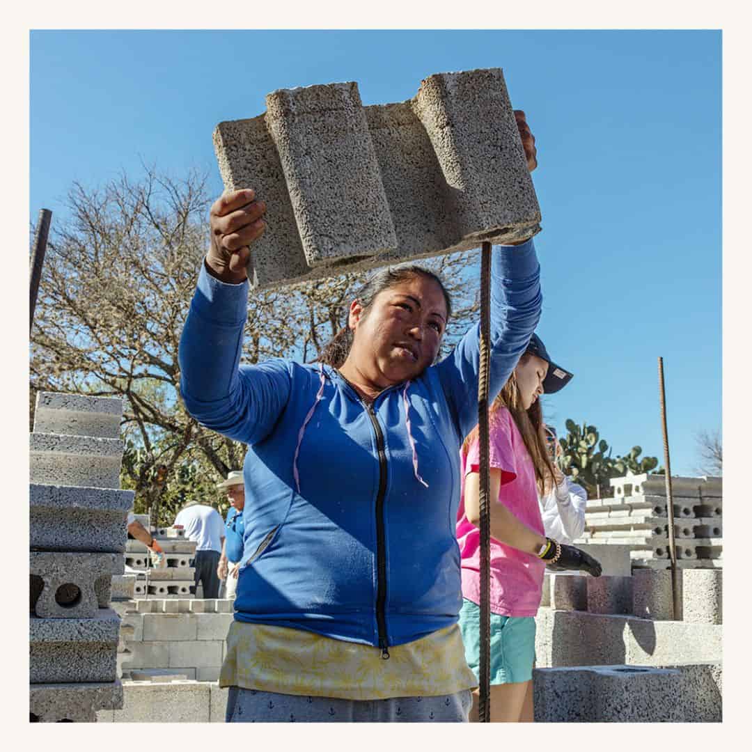 Mujer colocando bloque de concreto en construcción de viviendas.